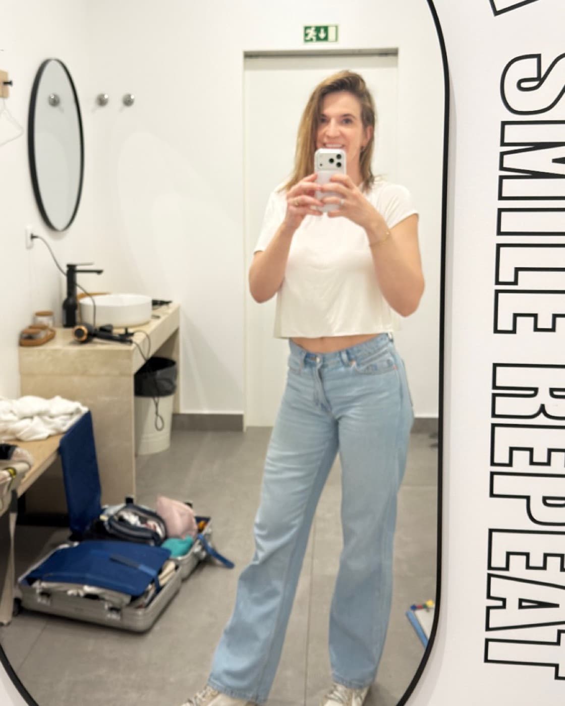 Angela im Umkleideraum vor dem Spiegel, Schriftzug „Lift Sweat Smile Repeat“ an der Wand